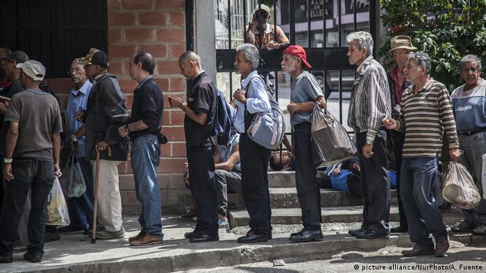 Hombres en Caracas haciendo cola ante una tienda de comestibles